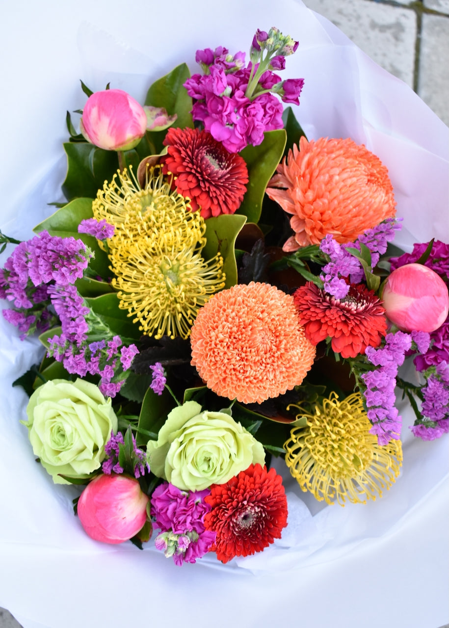 Bright &amp; colourful fresh flower bouquet. Created in colours of pink, bright orange, red &amp; lime green. Crafted by a florist &amp; presented in a white paper wrap.
