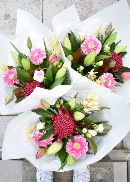 Three fresh flower bouquets in white paper wrap. Tulips, lilies and freesias in white and pink colours. Includes gerbera daisies and magnolia foliage.