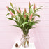 A glass vase of pink oriental lilies with winter Christmas foliage & Christmas with a Merry Christmas fabric ribbon